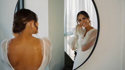 Woman in white shirt viewed from behind looking at her reflection in a round mirror.