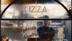 Pizza restaurant storefront window with neon signage and figure visible inside.