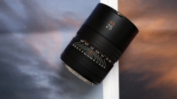 Black telephoto lens with focal length markings displayed against a dramatic cloudy sky backdrop.