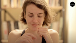 Woman with short blonde hair smiling with eyes closed, hand near face in contemplative pose.