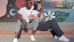 Two people sitting together against a colorful brick wall mural with street art.