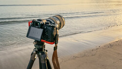 Professional camera on tripod mounted at beach during golden hour, facing ocean waves and shoreline.