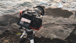 Mirrorless camera with telephoto lens mounted on tripod, positioned to frame ocean waves and rocky coastline.