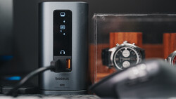 Baseus power strip with touch controls and orange digital watches displayed in background.