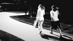 Two women jogging on a sunlit paved surface, captured in black and white with dramatic shadows.