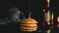 Stack of golden pancakes with syrup being drizzled over the top.