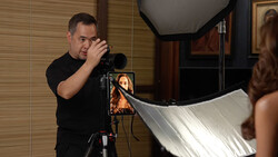 Photographer with camera on tripod positioning a reflector during a portrait lighting setup.