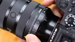 Close-up of a camera lens and camera body being held, showing focus ring and aperture markings.