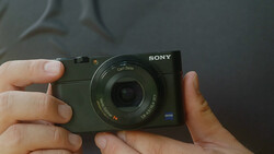 Hands holding a Sony compact camera with Zeiss lens and blue accent detail.
