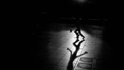 Silhouette of a person in dynamic pose with dramatic shadow cast on tiled floor in low-light setting.