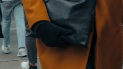 Person wearing a mustard-yellow coat and black leather gloves holding a dark textured handbag.