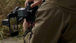 Photographer holding a DSLR camera with external monitor displaying live view footage in outdoor setting.