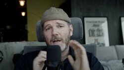 Man speaking into a microphone while wearing a beanie cap in a studio setting.
