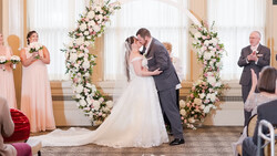 Bride and groom kiss at the altar beneath a floral arch during wedding ceremony.