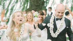 Bride and groom walk together under a canopy of hanging greenery during their wedding ceremony.