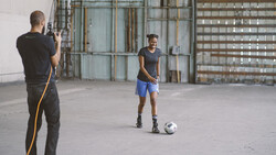Photographer shooting a soccer player posing with a ball in an industrial space.