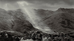 Dramatic mountain valley with crepuscular rays breaking through storm clouds over a winding river.