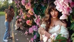 Woman in off-shoulder white dress posing among blooming pink flowers during outdoor portrait session.