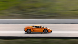 Orange sports car in profile against blurred green and gray background.