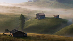 Misty alpine valley with scattered wooden chalets nestled among rolling green hills at golden hour.