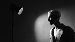 Male subject in profile against dark background, illuminated by studio lighting from the left side.