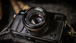 Vintage rangefinder camera with Fujinon lens mounted on dark leather strap against textured background.