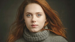 Portrait of a young woman with copper-red hair wearing a gray turtleneck sweater.