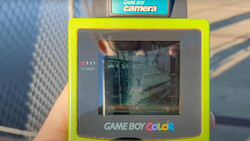 Game Boy Color camera accessory with bright yellow frame displaying interior hallway scene on screen.