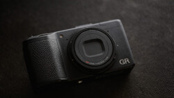 Ricoh GR compact camera with fixed lens on dark textured surface.