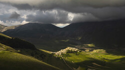 Alpine valley village nestled between forested mountain slopes under dramatic storm clouds.