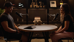 Two people sitting at a round table with microphones in a podcast studio setup.
