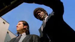 Two men in dark suits photographed from below against a clear blue sky.