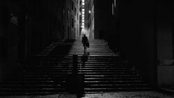 Solitary figure walking up a long staircase in a narrow alley, rendered in high-contrast black and white.
