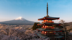 Red pagoda with snow-covered trees and snow-capped mountain in background under clear blue sky.