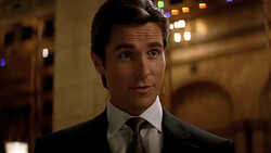 Man in formal dark suit and tie looking directly at camera with slight expression indoors.