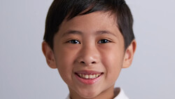 Young boy with dark hair smiling at camera against neutral gray background.