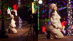 Woman in white fur coat kneeling among colorful holiday lights during a studio photo shoot.