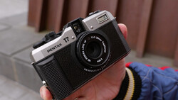 Pentax 17 film camera held in hand, showing chrome top plate and black body with textured grip.