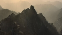 Misty mountain peaks silhouetted against hazy golden light filtering through atmospheric layers.