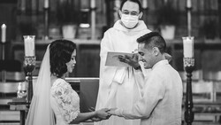 Bride and groom exchange rings at altar while priest holds ceremonial book during church wedding ceremony.