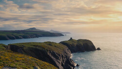 Dramatic coastal cliffs and headlands overlooking calm sea under golden-hour sky.