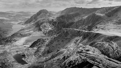 Mountain lakes nestled in a rocky alpine valley with winding road visible on distant ridge.
