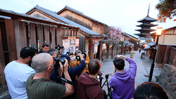 Group of photographers with cameras photographing a traditional Japanese street lined with wooden buildings and a pagoda in the background.
