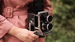 Person in rose-colored jacket holding a twin-lens reflex camera with dual objectives and viewfinder.