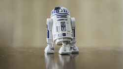 R2-D2 droid action figure photographed on a reflective surface against a soft neutral background.