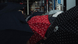Colorful polka-dotted umbrellas held up during rain in an urban street setting.