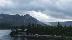 A snow-capped mountain peak rises behind a forested shoreline with a small waterfront cabin and dock.