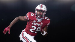 Football player in maroon uniform number 29 in athletic stance against dark background.