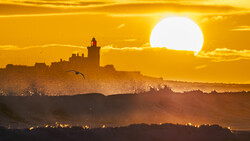 Silhouetted cityscape with cathedral at sunset, large sun behind golden sky and haze.