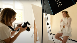 Photographer holding a camera while shooting a model in a studio setting with professional lighting equipment.